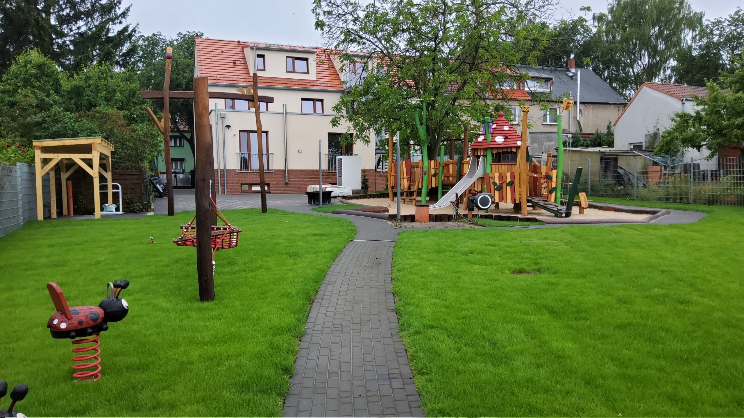 Spielplatz einer Kita mit Klettergerüst, Rutsche, Schaukeln und grünem Rasen