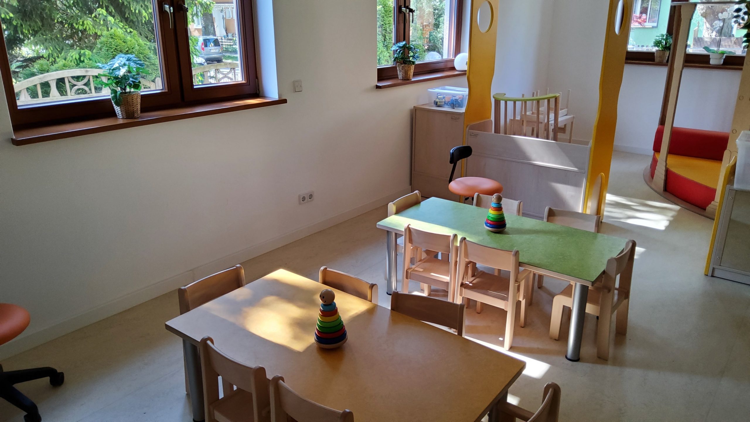 Innenraum einer Kita mit kleinen Tischen und Stühlen, Spielzeug und freundlicher Tageslichtbeleuchtung