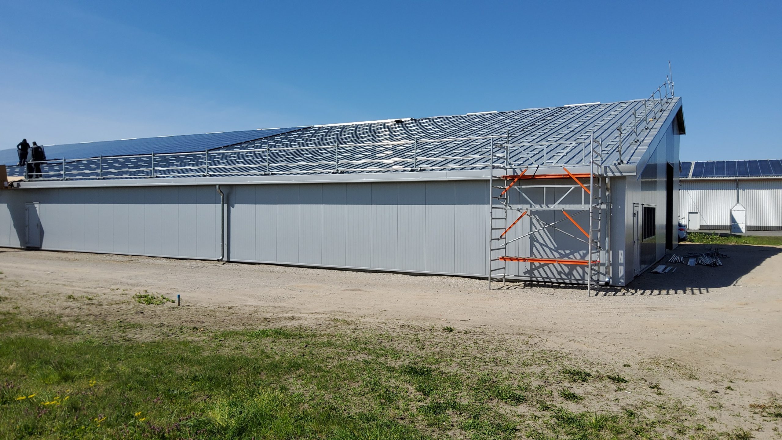 Lagerhalle im Ausbau mit bereits montierter Wandverkleidung und laufender Dachmontage – betreutes Bauprojekt mit Sicherheitsgerüst