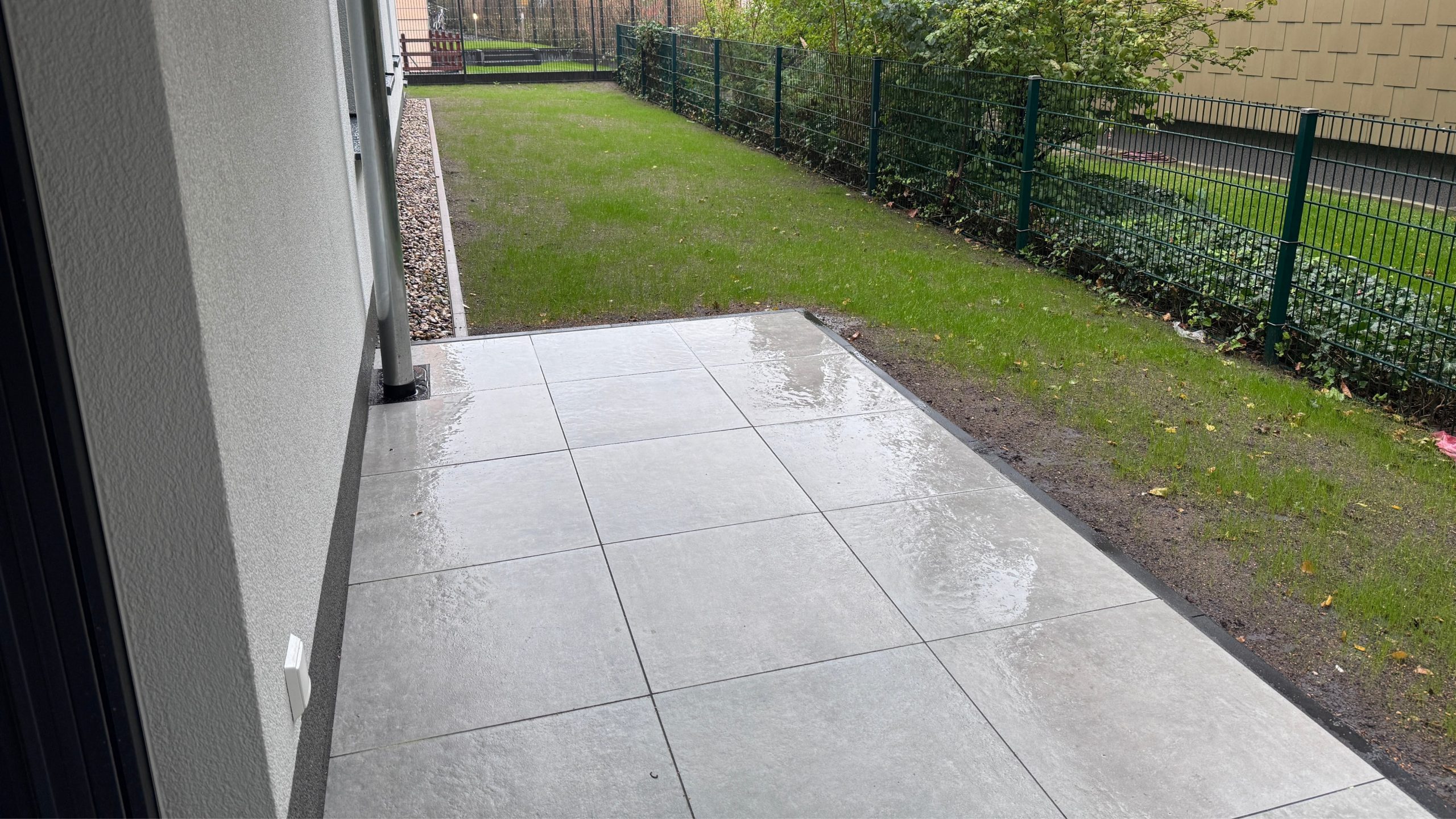 Terrasse mit hellen Bodenplatten und angrenzendem Rasen im fertiggestellten Wohnbauprojekt von Niehof Bautechnik