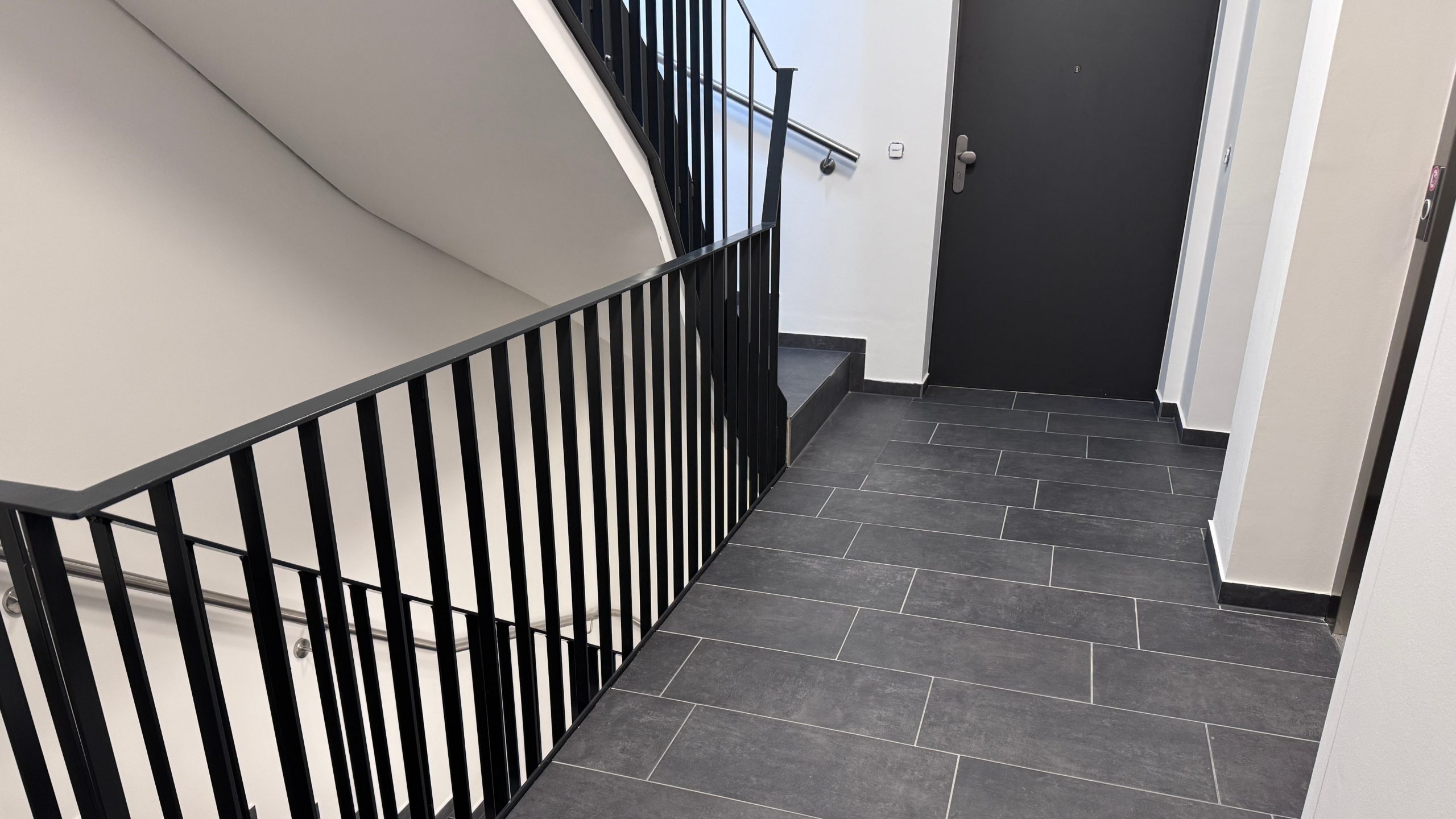 Treppenhaus mit schwarzem Metallgeländer und dunklem Fliesenboden im Neubauprojekt von Niehof Bautechnik
