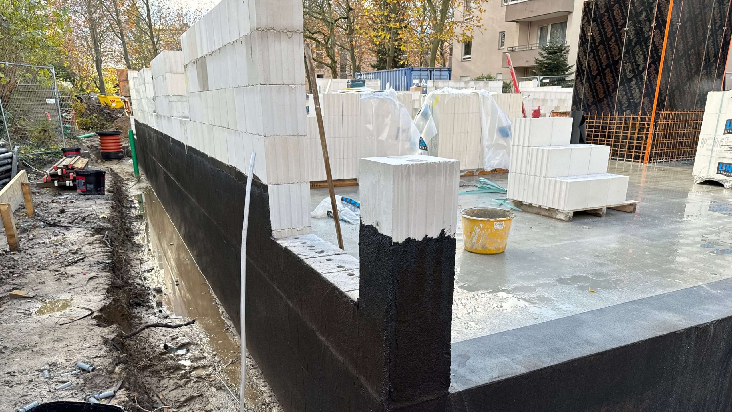 Betreutes Bauprojekt im Rohbau: Frisch gemauerter Wandaufbau mit schwarzer Abdichtung und weißen Kalksandsteinen auf Baustelle eines Mehrfamilienhauses