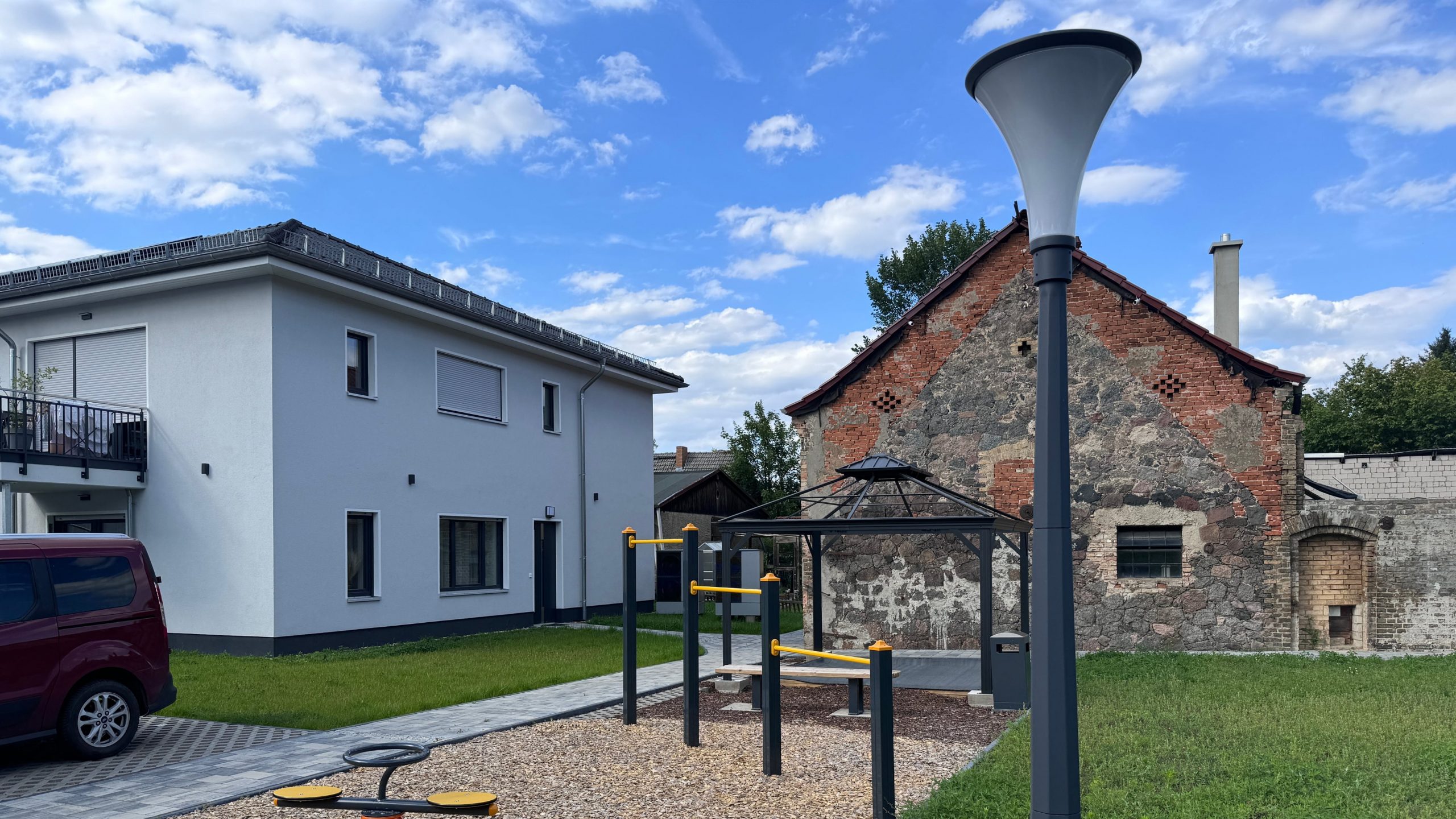 Außenbereich eines betreuten Neubauprojekts mit modernem Wohnhaus, historischem Bestandsgebäude und Spiel- oder Fitnessbereich