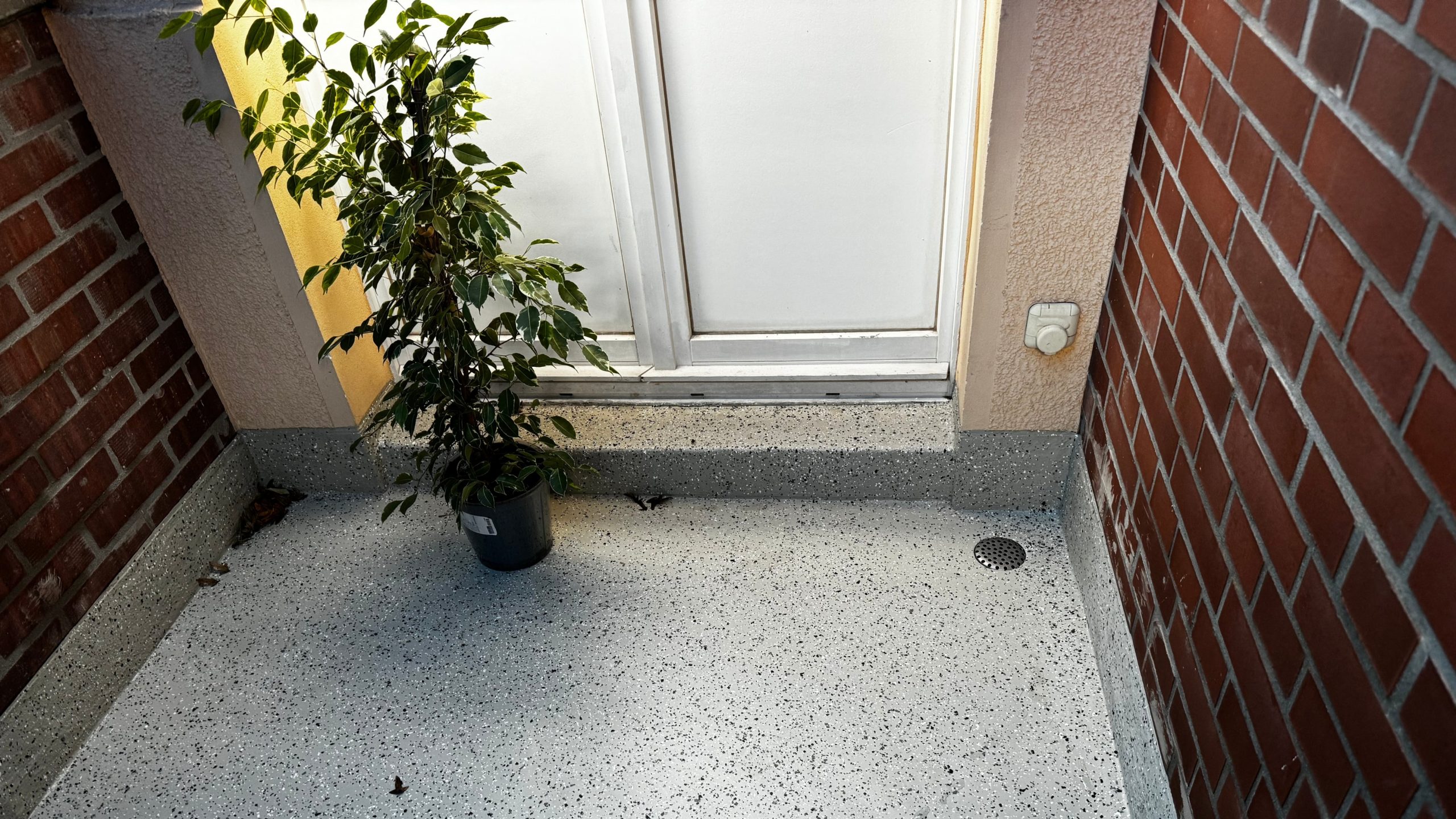 Sanierter Balkon mit hellgrauem, fugenlosen Beschichtungsbelag und moderner Entwässerung