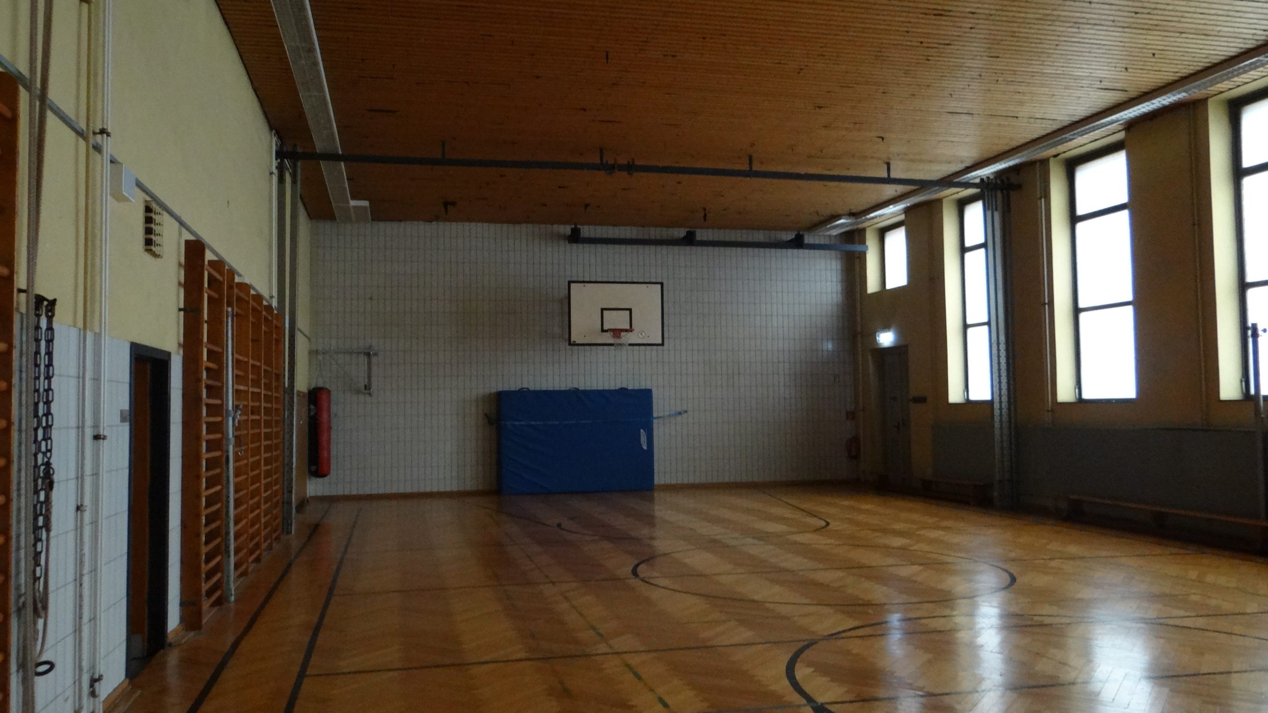 Sporthalle vor der Sanierung mit altem Holzfußboden, Fliesenwänden und veralteter Ausstattung