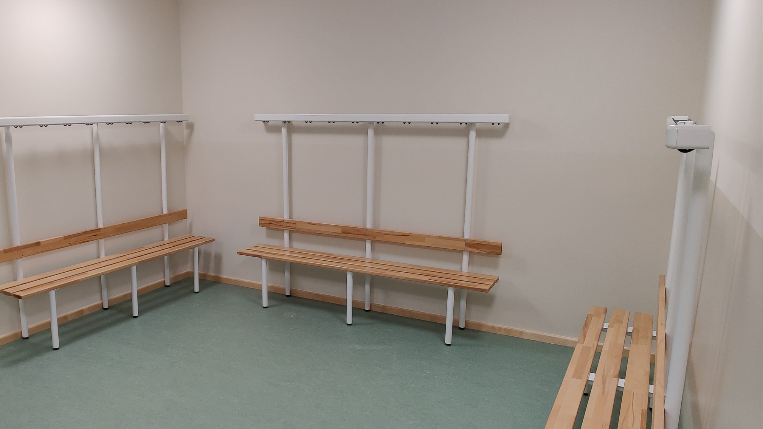 Modern sanierter Umkleideraum mit Holzbänken und Garderobenhaken im Bauprojekt einer Sporthalle