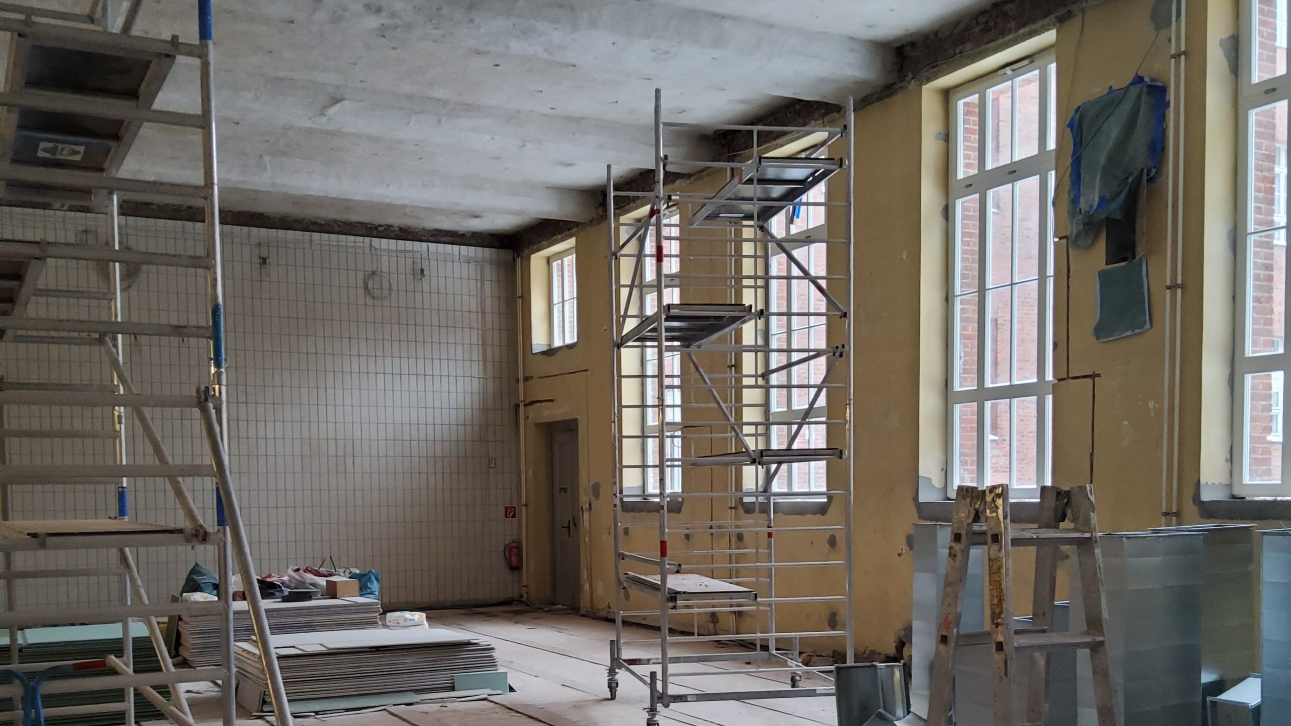Sanierung einer Sporthalle mit Gerüsten, Baumaterialien und offenen Wandflächen im Rahmen eines betreuten Bauprojekts
