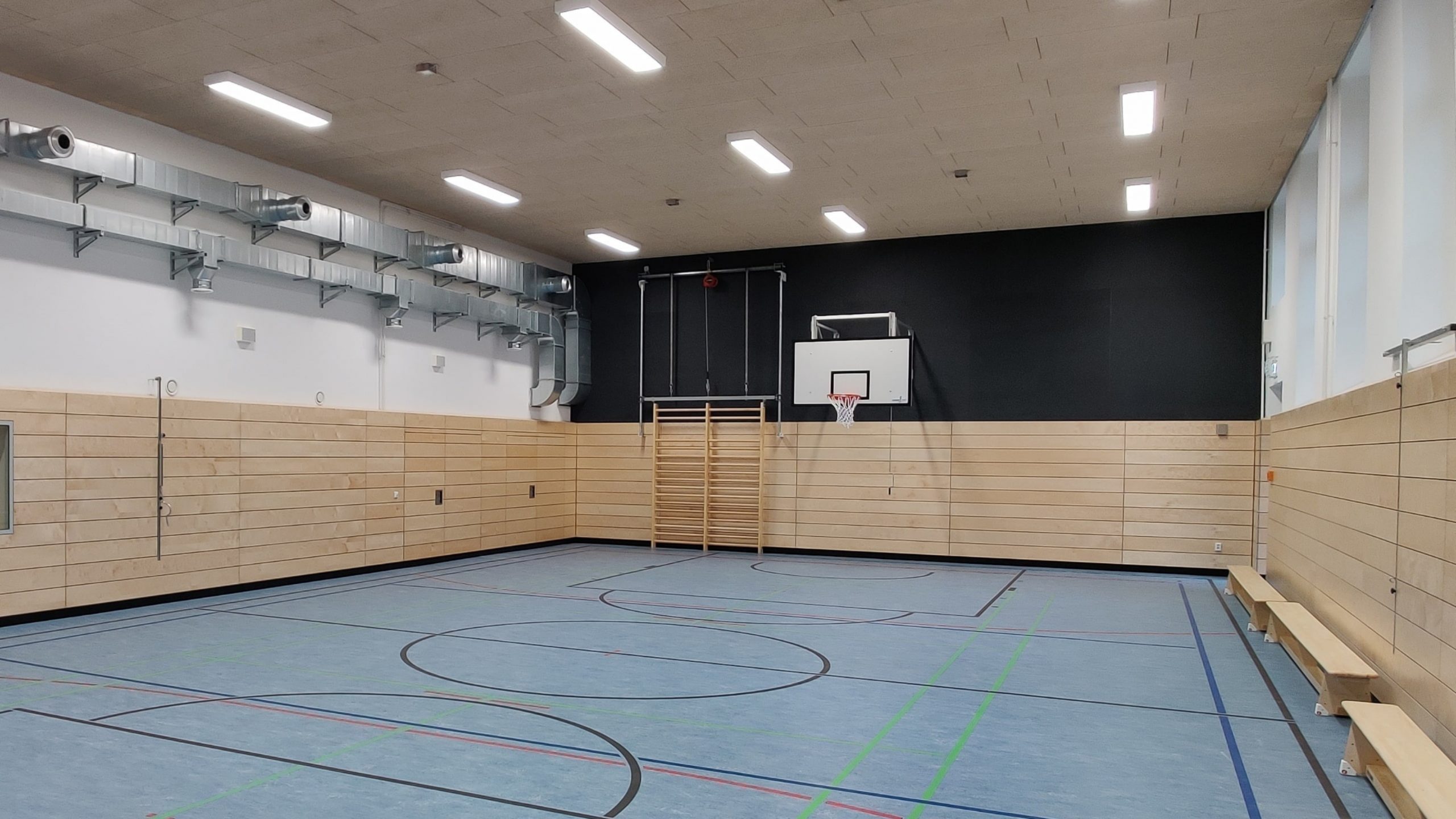 Modernisierte Sporthalle mit neuem Bodenbelag, heller Wandverkleidung, Lüftungsanlage und Basketballkorb nach der Sanierung